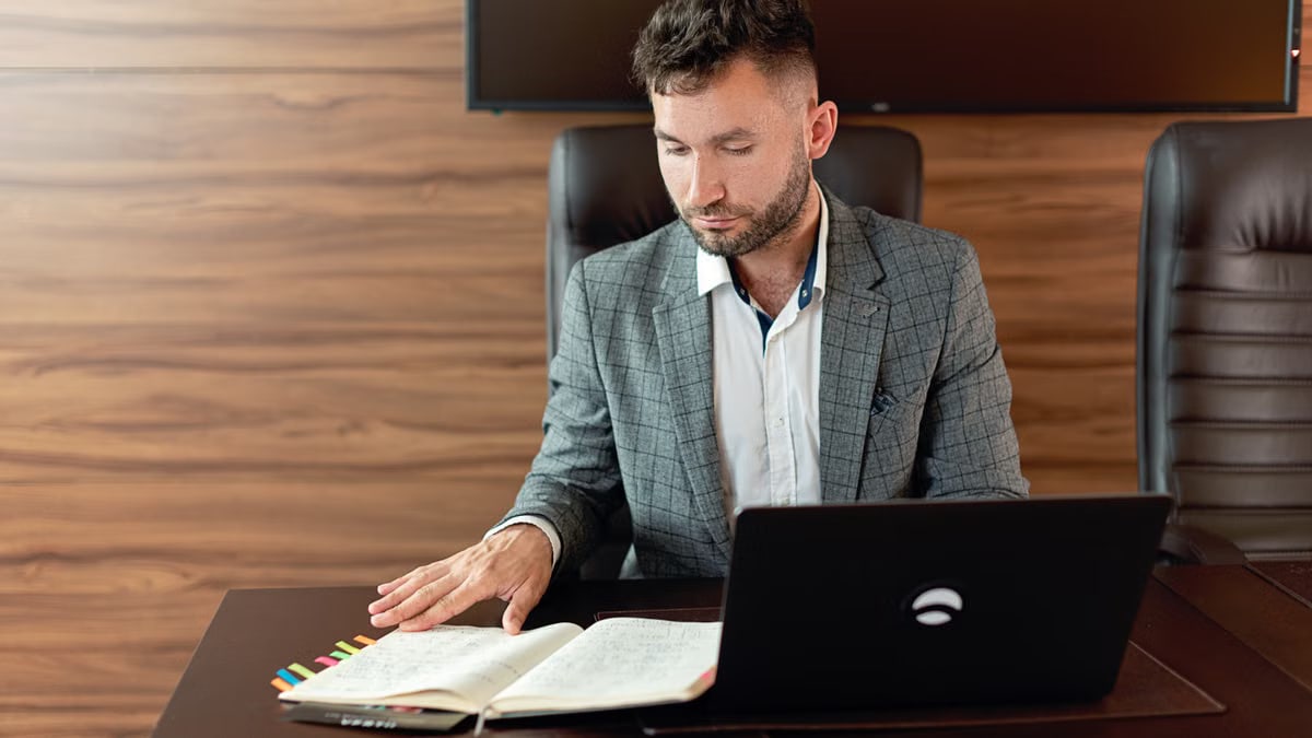 Focused man working on laptop and notes in a modern office.